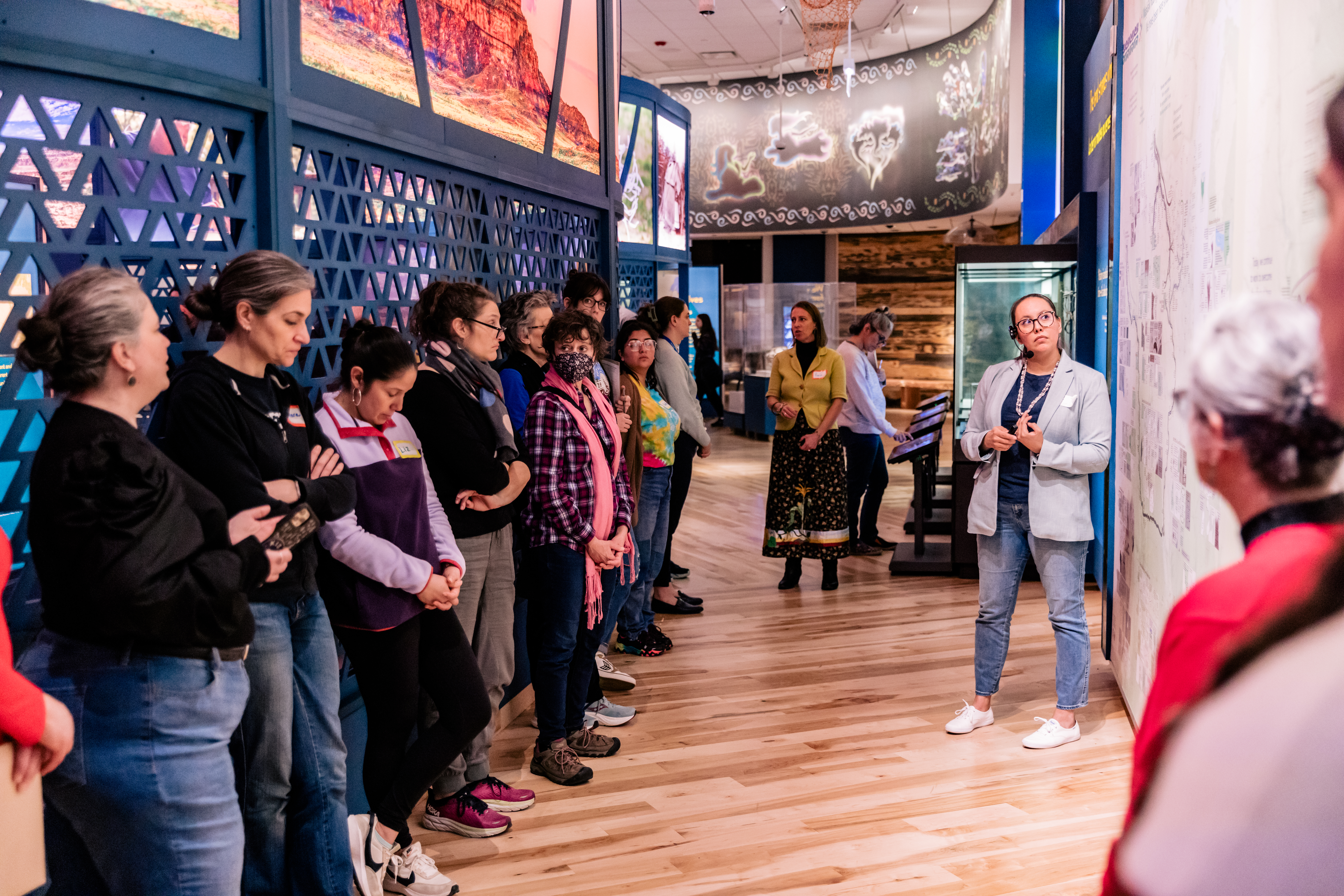 A group of educators stands looking at a museum display as staff presents the content.