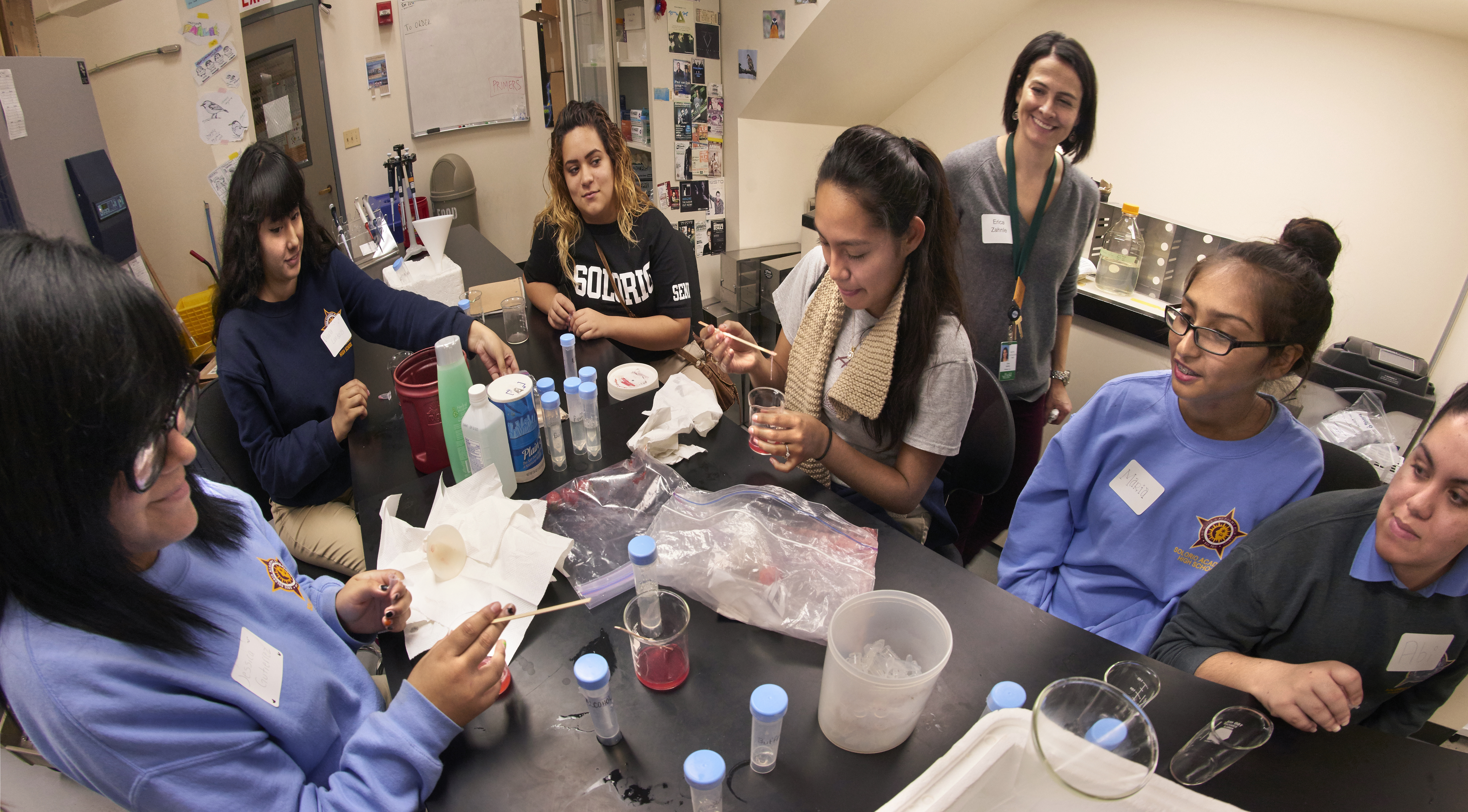 Five high school students sit around a lab table performing an experiment with Field Museum scientist Erica Zahnle.