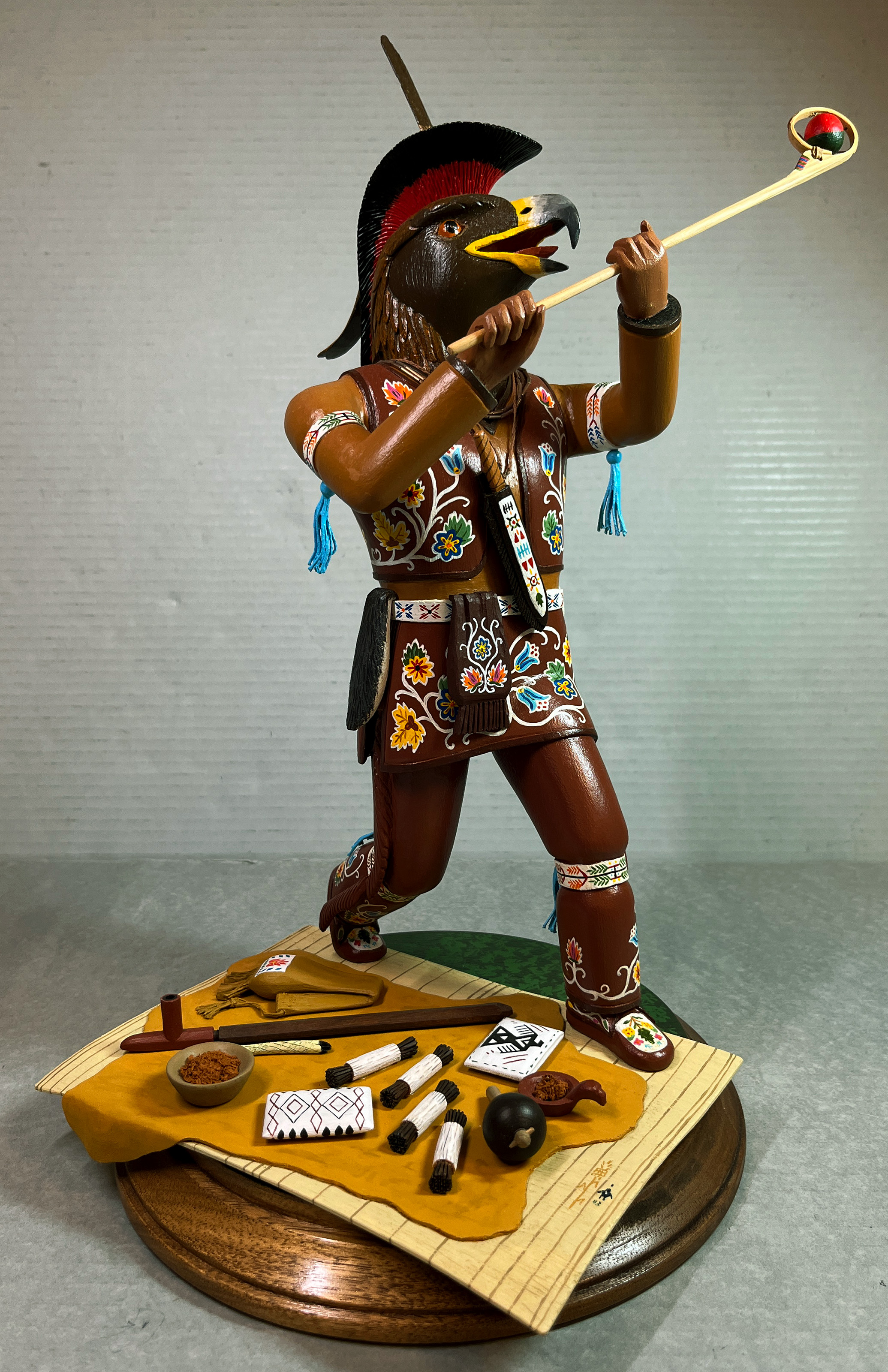A colorfully painted totem of a golden eagle person holding a lacrosse stick with a ball in it.