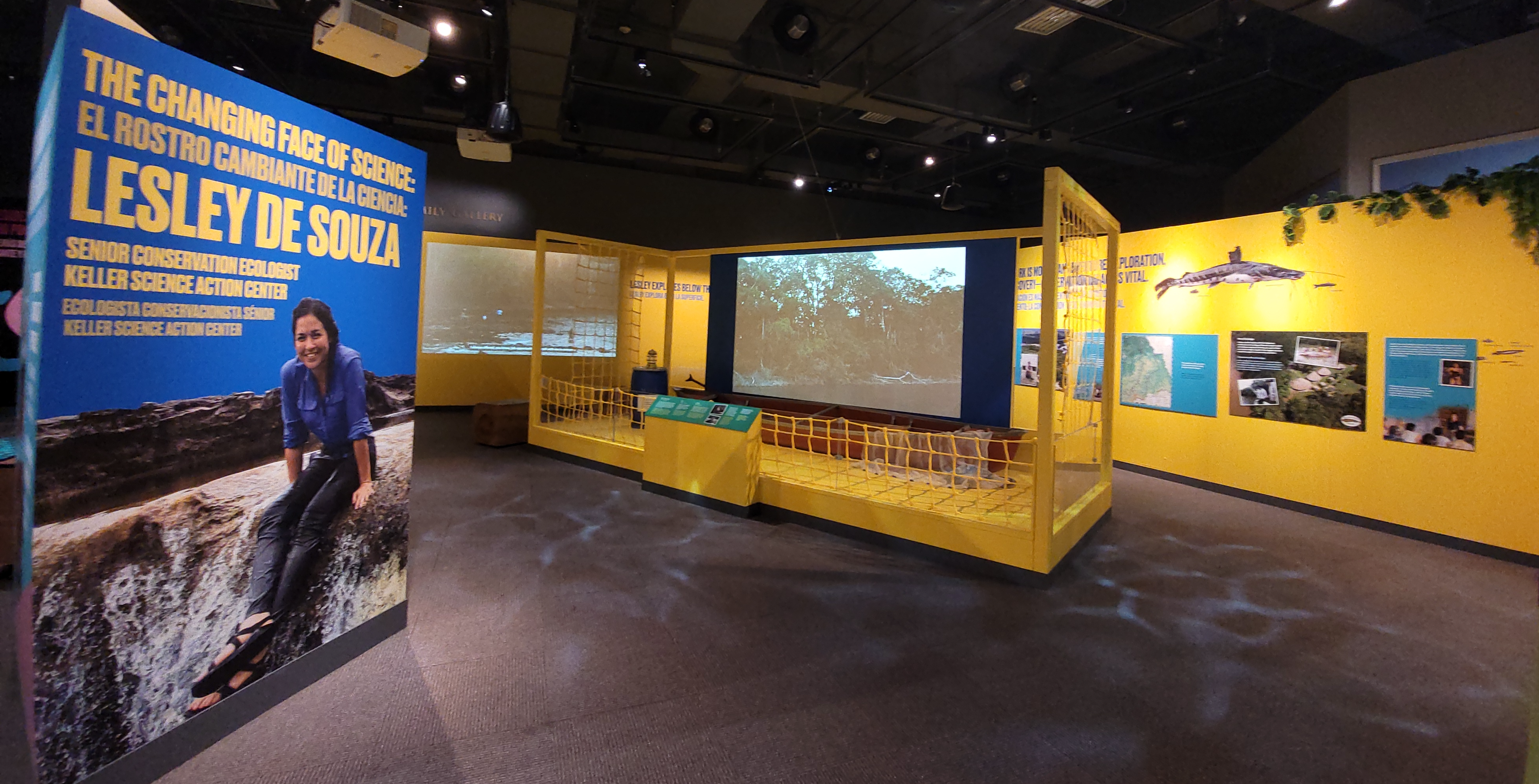 A museum exhibition space with large video screens and graphic panels.