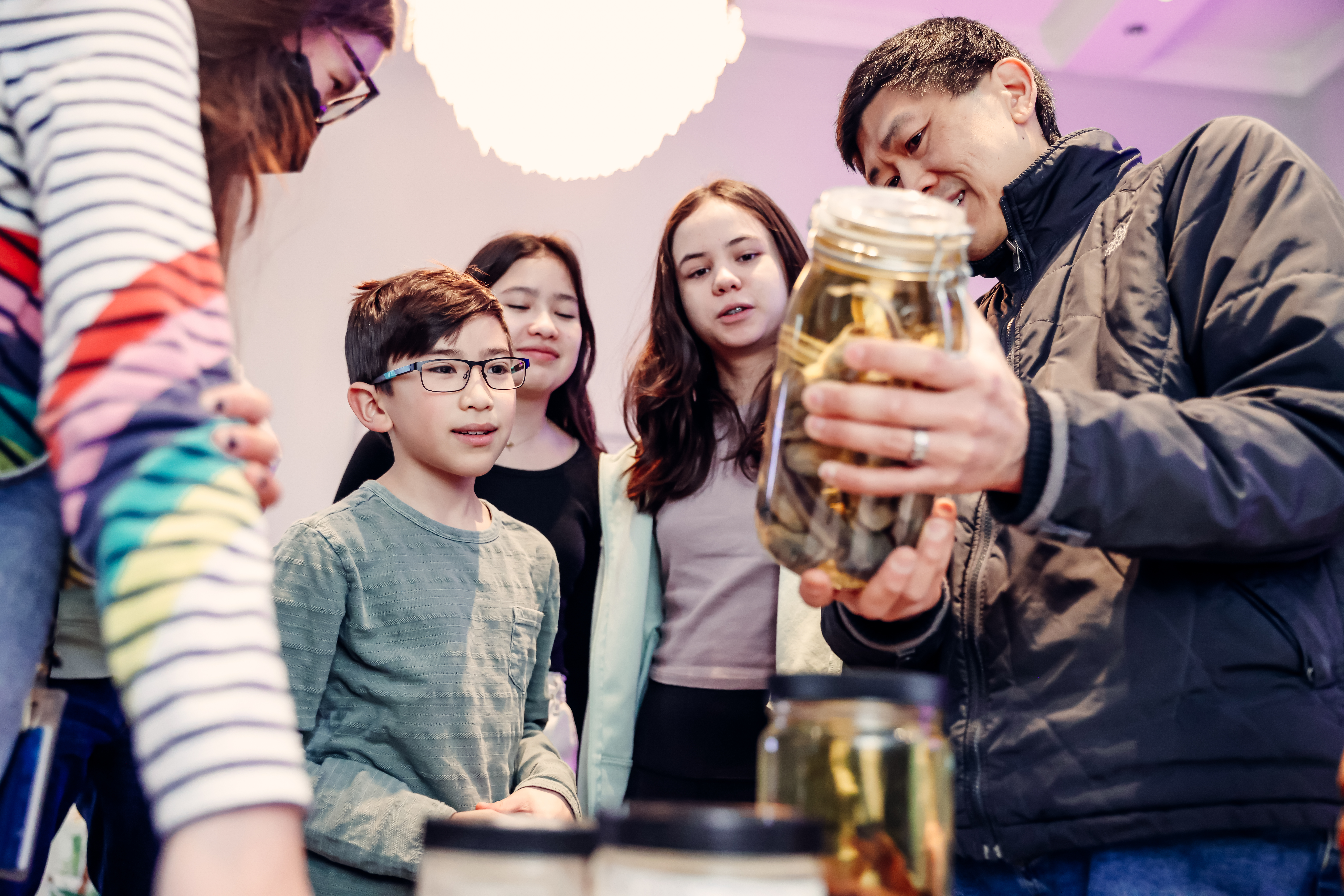A man holds a specimen jar of fish up for children to view.