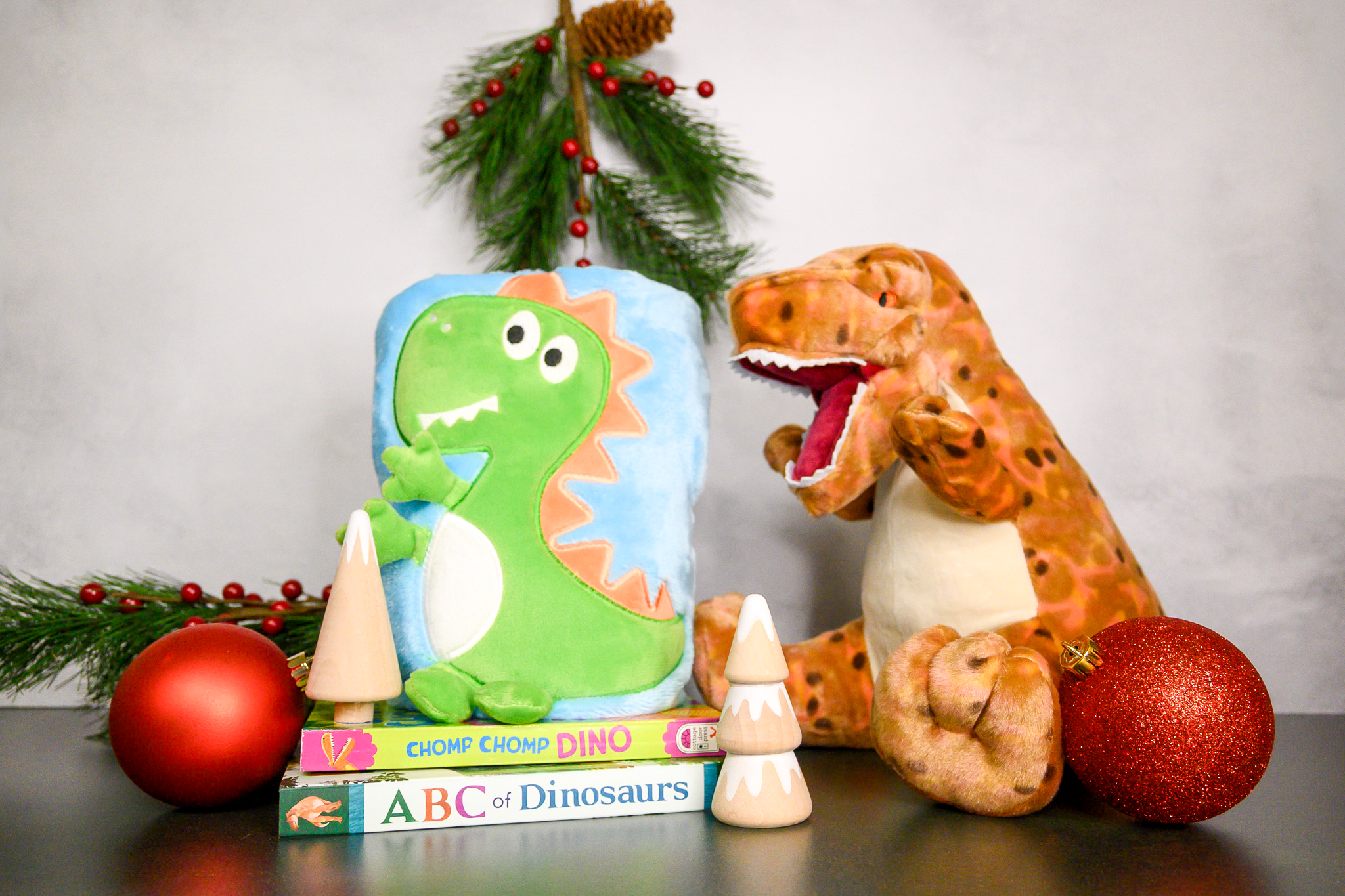 A T. rex plush dinosaur, cozy baby blanket with a cartoon dinosaur, and two books: Chomp Chomp Dino and ABC of Dinosaurs