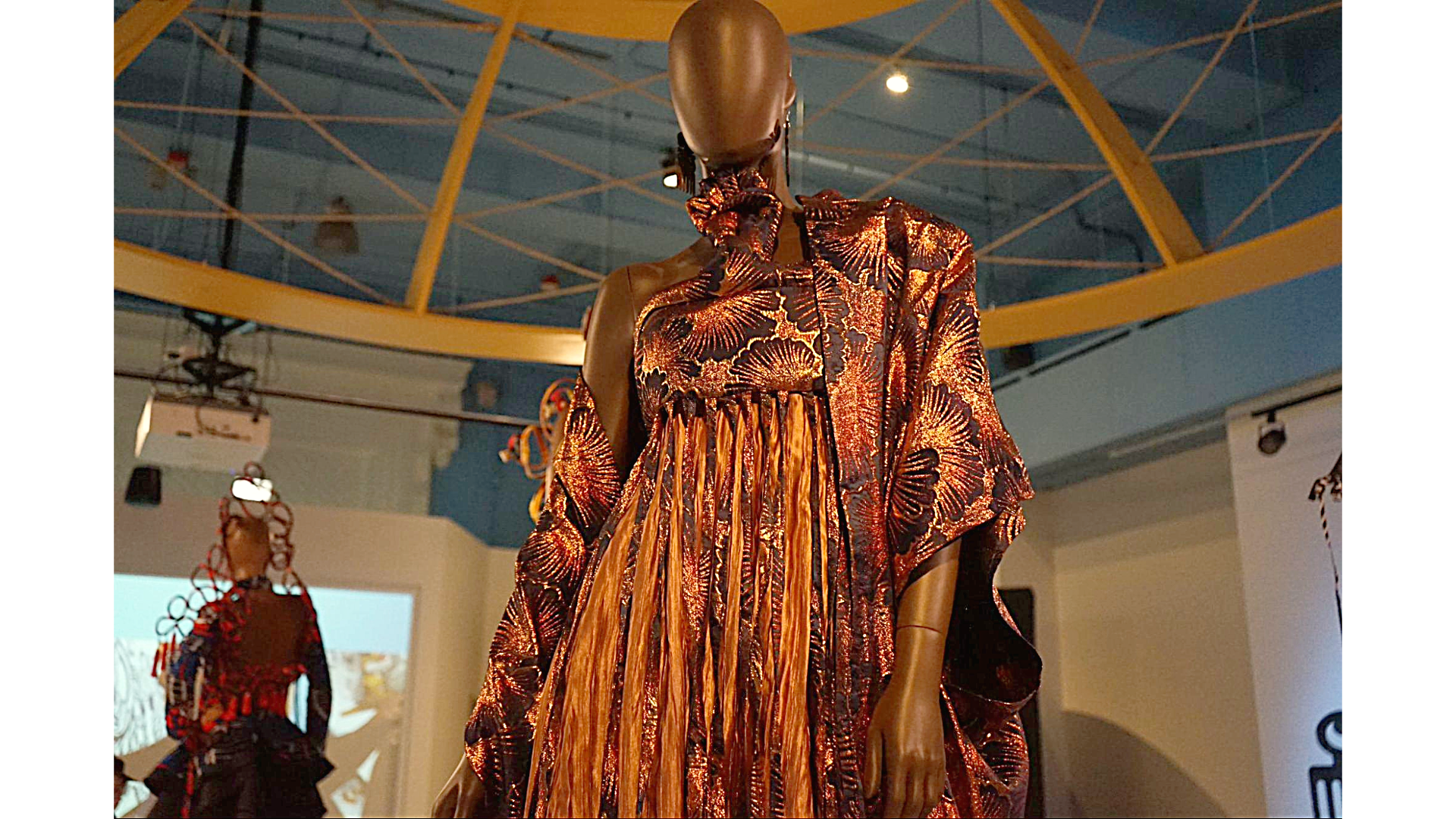 A gold and purple garment with cascading strands of fabric, on a mannequin