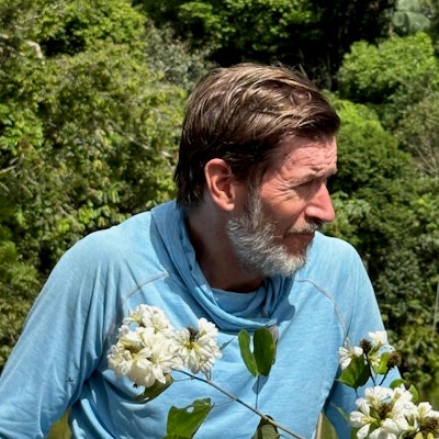 Nigel Pitman in profile in front of trees and behind flowers