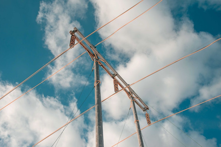 a view of power lines from below, clouds in a blue sky