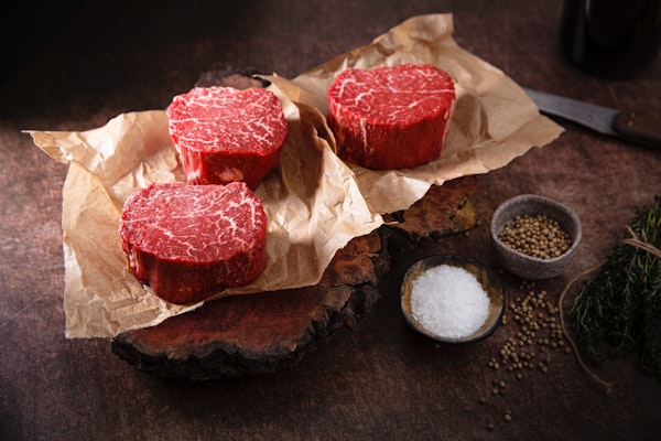 Three beef steaks on a countertop, with bowls of salt and pepper next to them