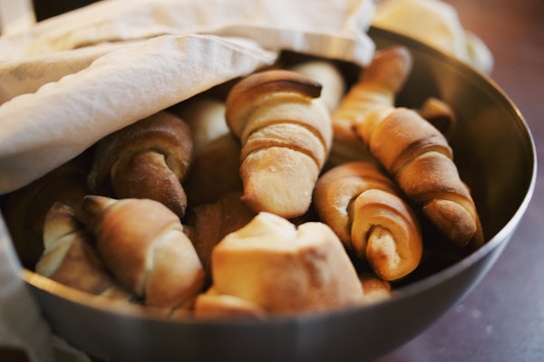 A metal bowl of crescent rolls half covered by a flour sack towel