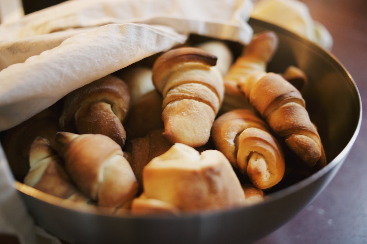 A metal bowl of crescent rolls half covered by a flour sack towel