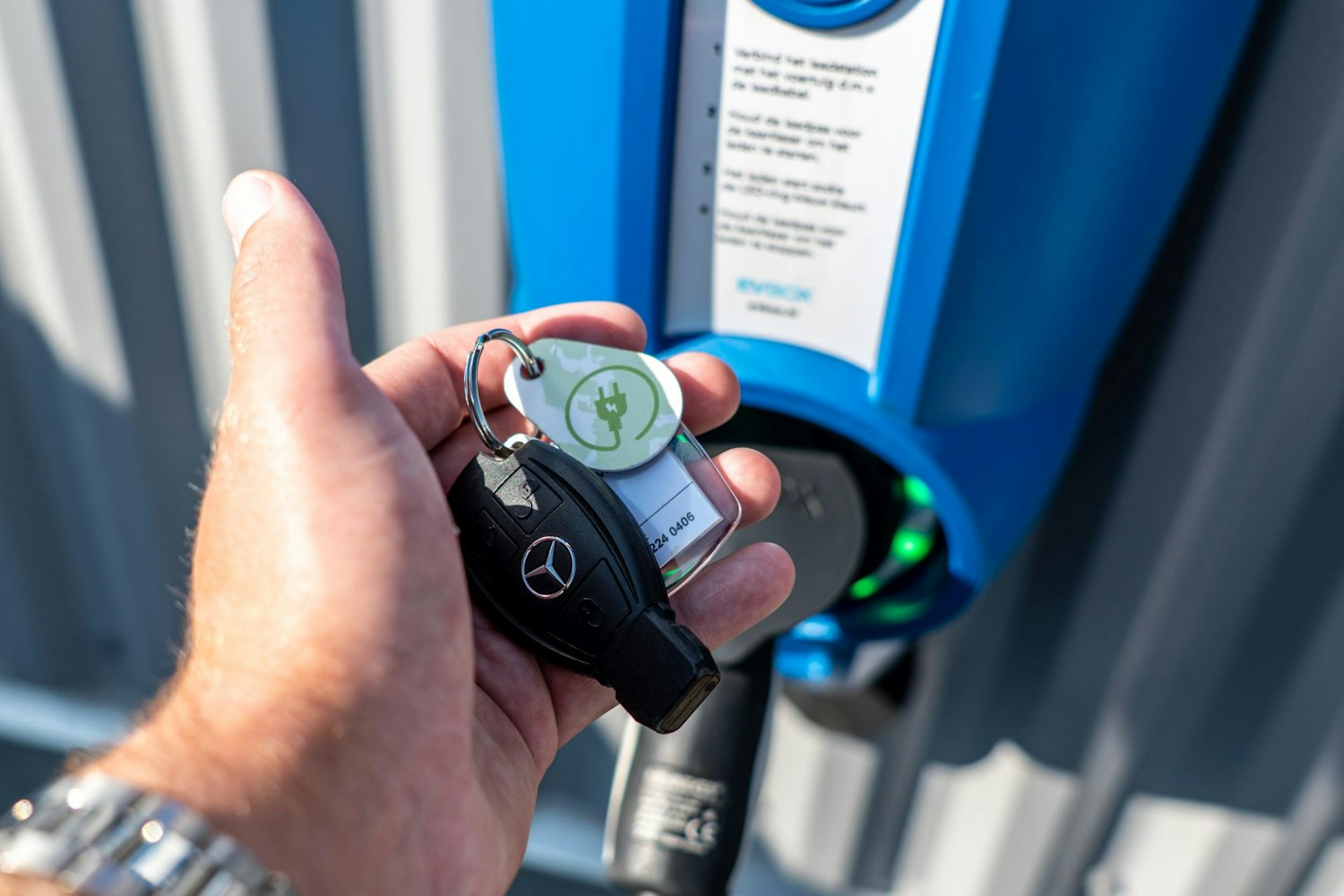 Autosleutels met laaddruppel in een hand voor een elektrische laadpaal.