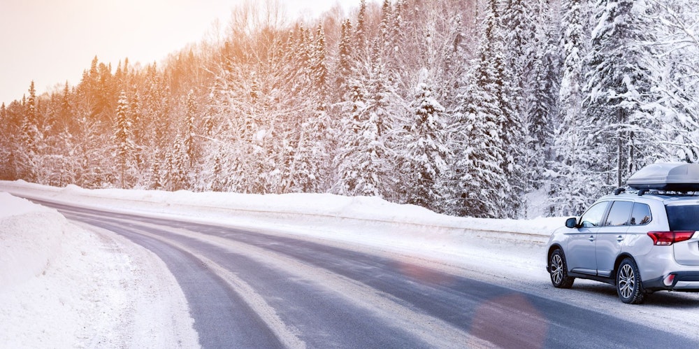 Auto met dakkoffer rijdt op een besneeuwde weg door een bos.