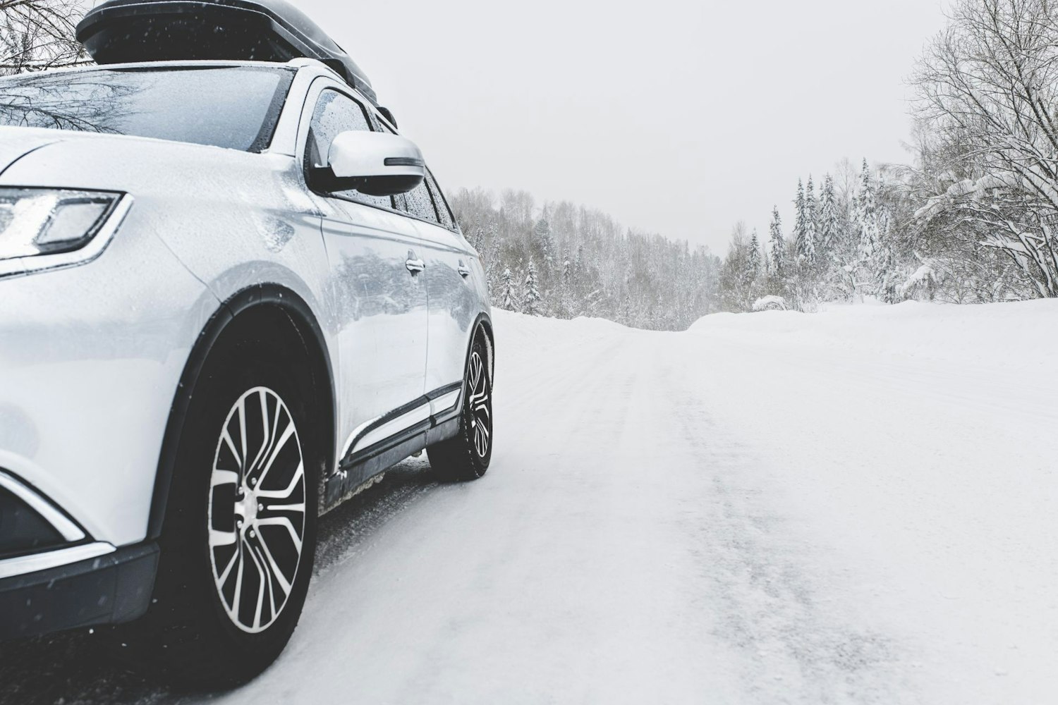 Auto met dakkoffer op een met sneeuw bedekte weg.