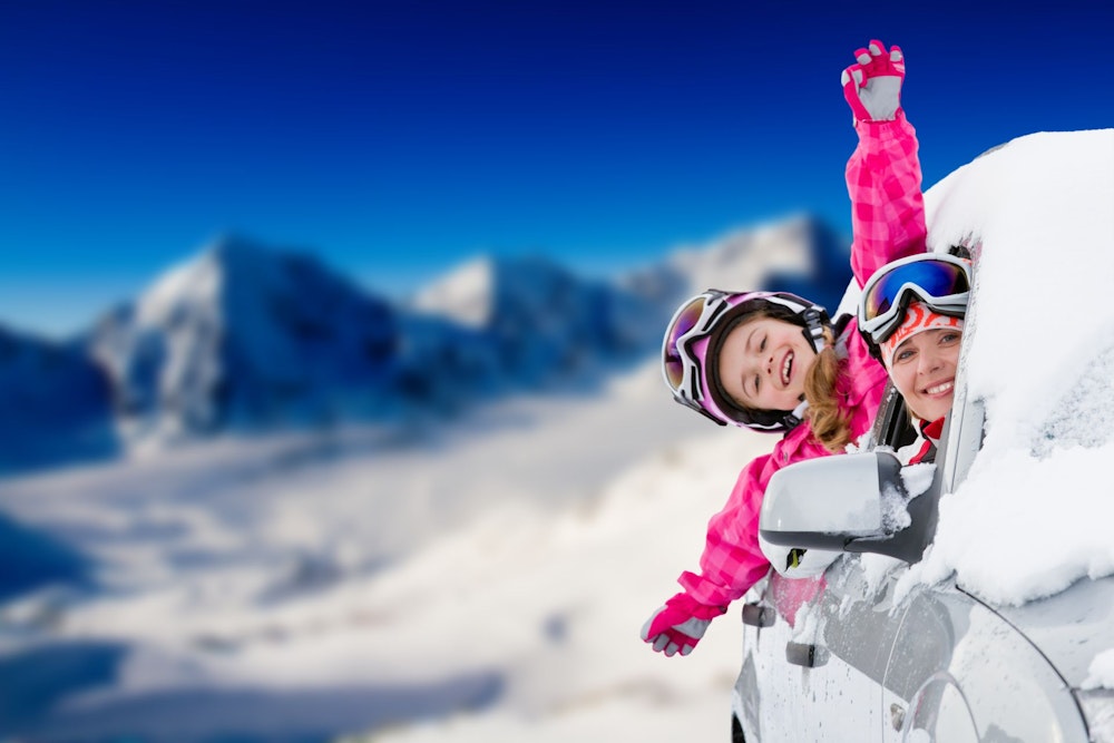 Mother and daughter hang out from snow-covered car in the mountains.