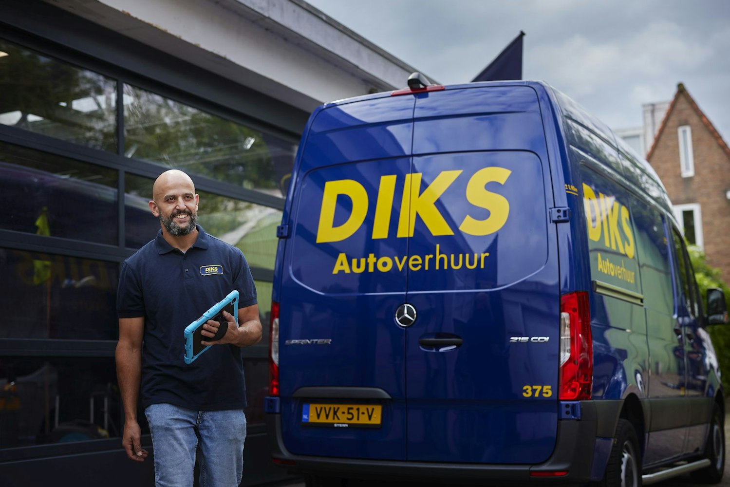 Man loopt met tablet achter blauwe bestelbus van DIKS autoverhuur langs.