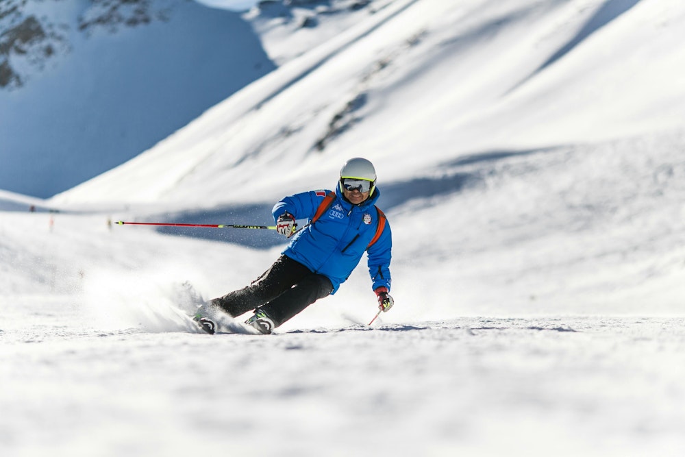 Skiér in blauwe jas en witte helm op de piste in de sneeuw.