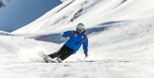 Skiér in blauwe jas en witte helm op de piste in de sneeuw.