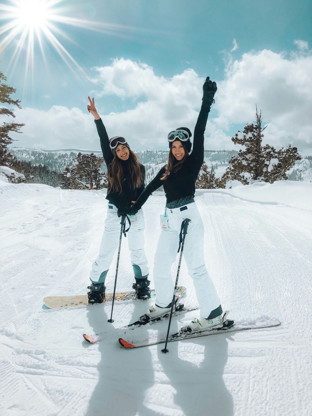 Twee lachende meiden op ski's en een snowboard in de sneeuw.