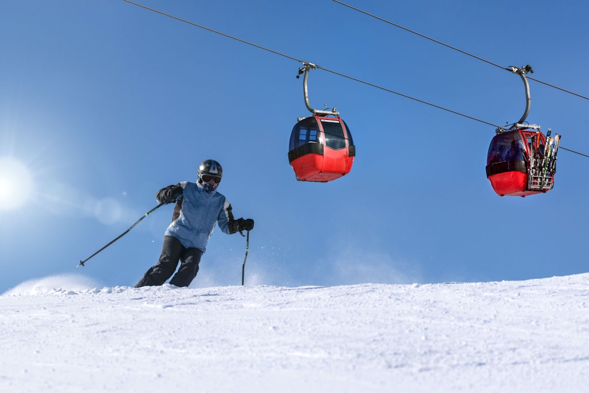 Man op ski's in de sneeuw met op de achtergrond twee rode skiliften.