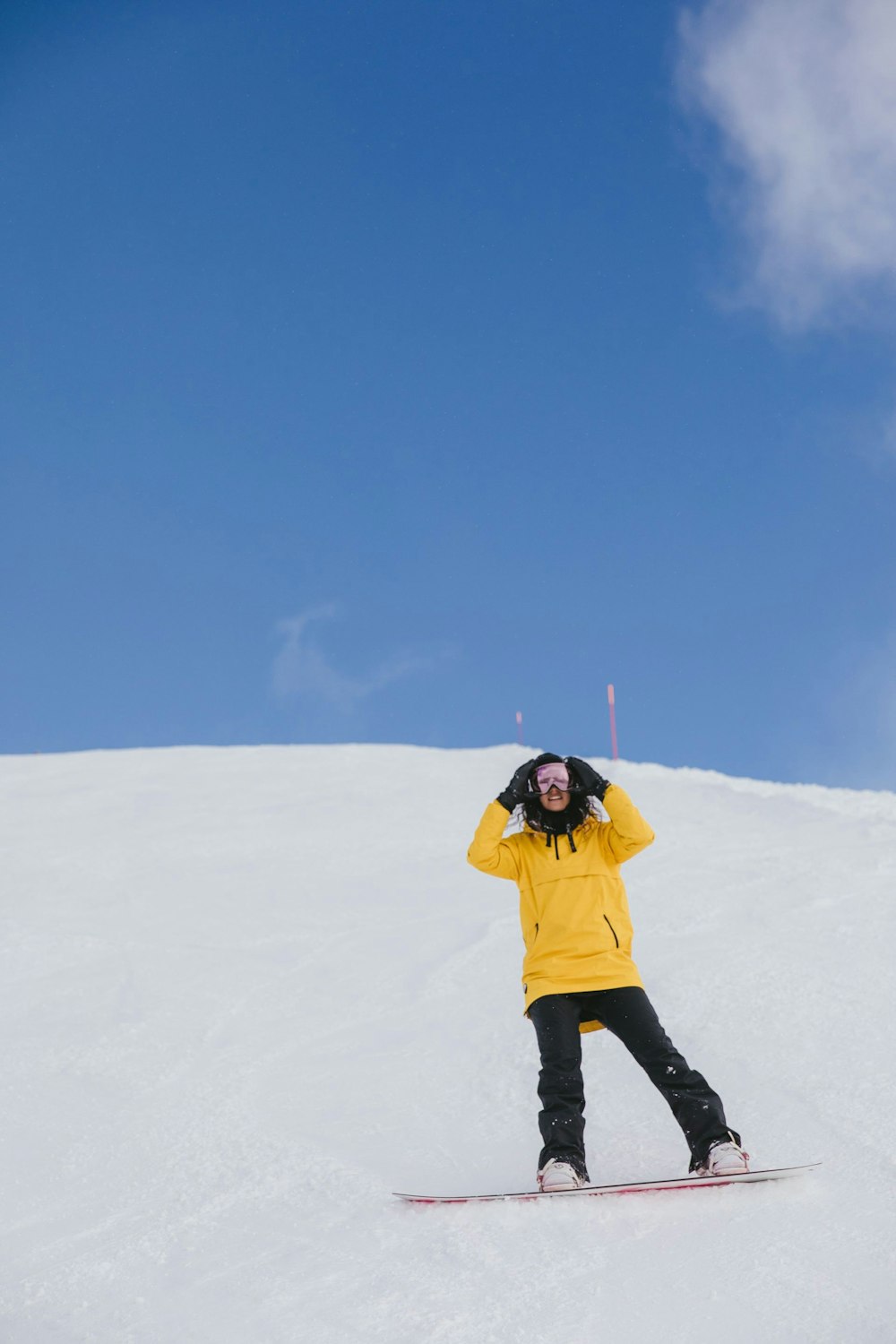 Meisje met gele jas op een roze snowboard op een skipiste met blauwe lucht.