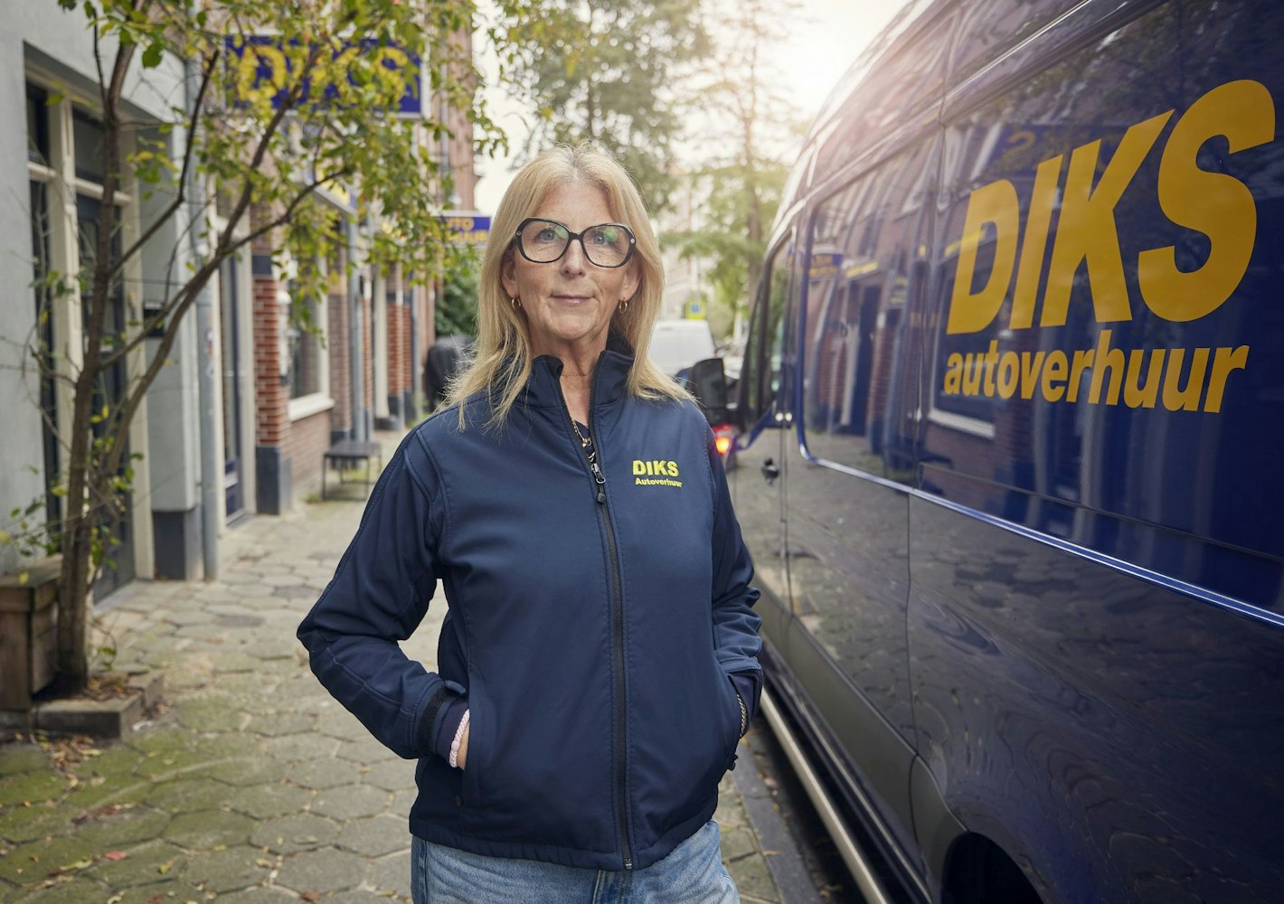 DIKS medewerkster staat voor busje met DIKS logo bij een vestiging in Amsterdam Zuid.