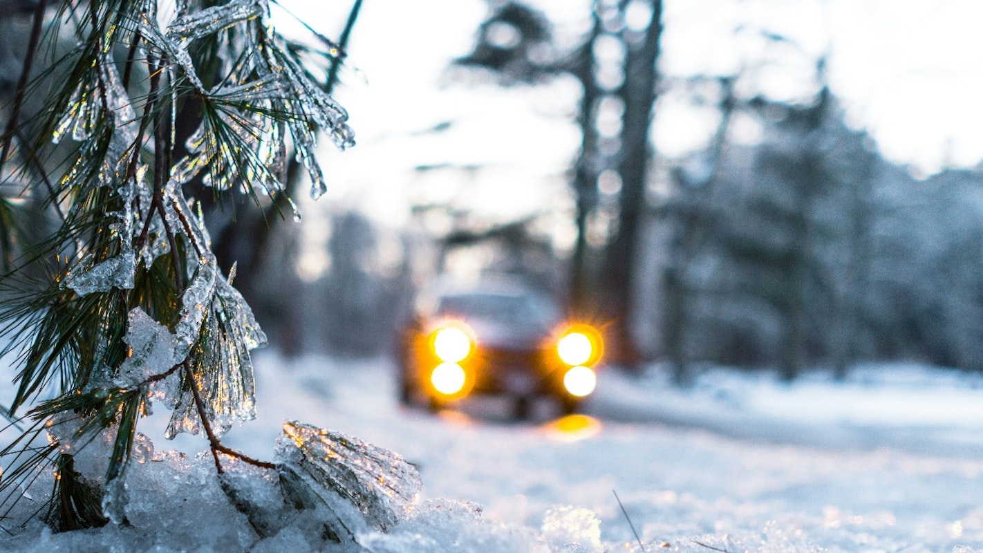 Auto met winterbanden  en brandende koplampen rijdt over een besneeuwde weg.