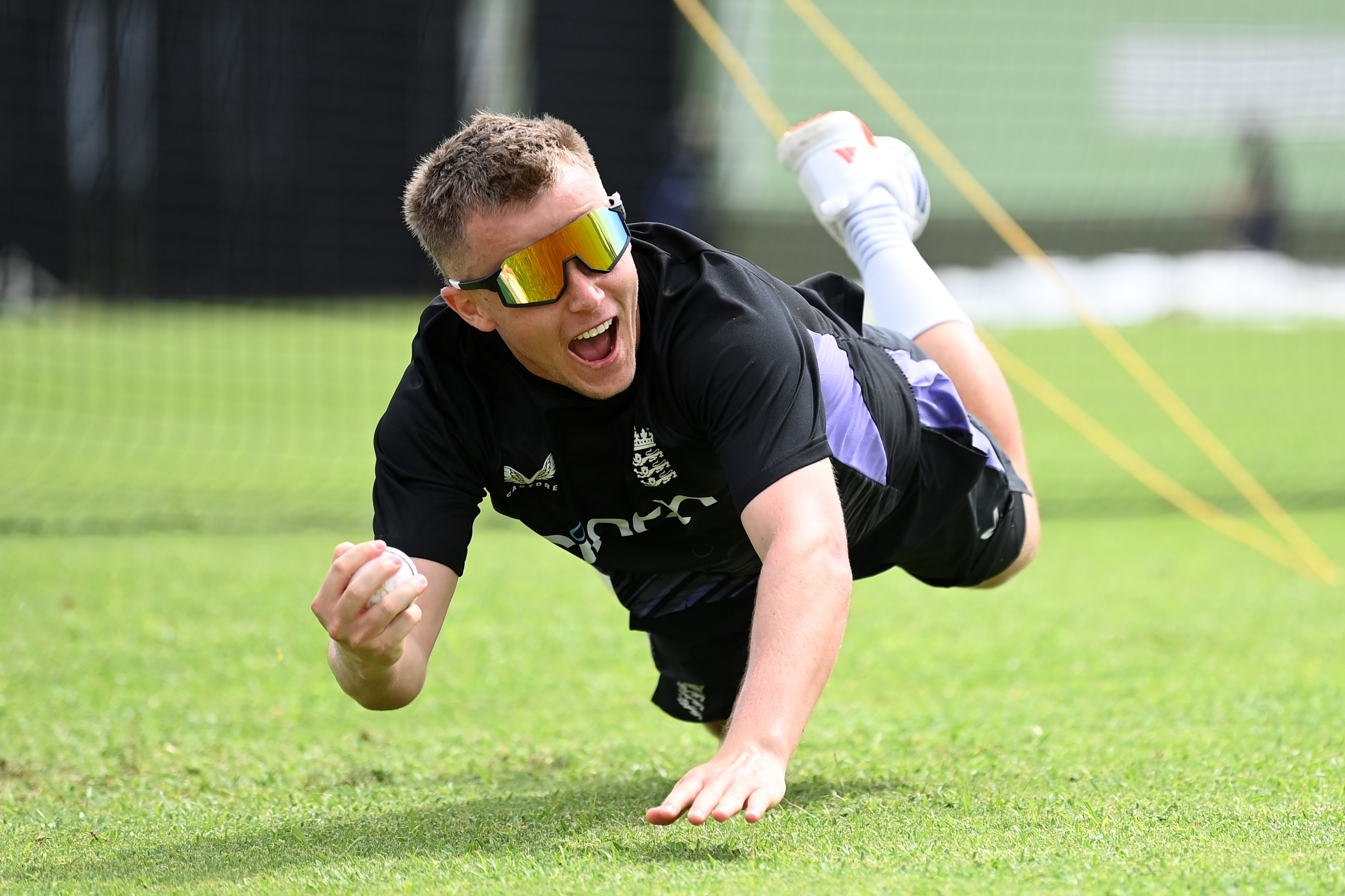 Player catching a cricket ball while falling on the ground