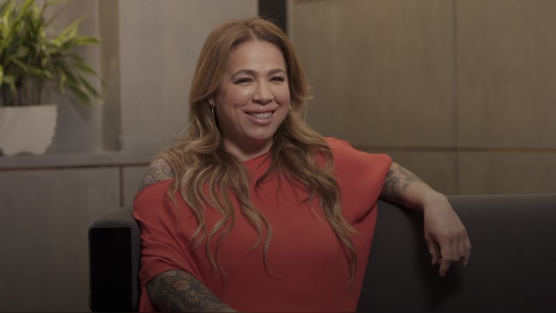 video still of a patient smiling in an orange top sitting on a couch