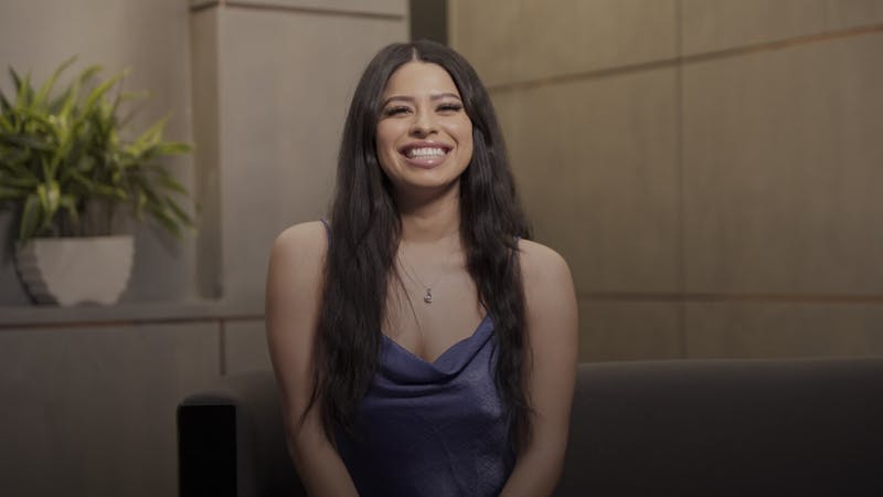 a video still of a dark haired patient smiling in a purple top