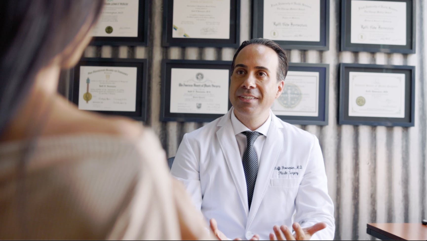 Dr. Hovsepian talking to a patient in his office with awards on the wall