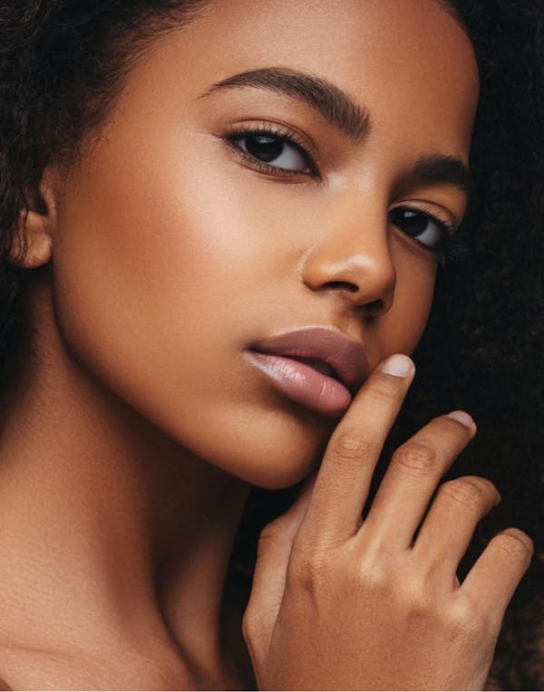 Beautiful woman with clear skin touching her hand to her mouth
