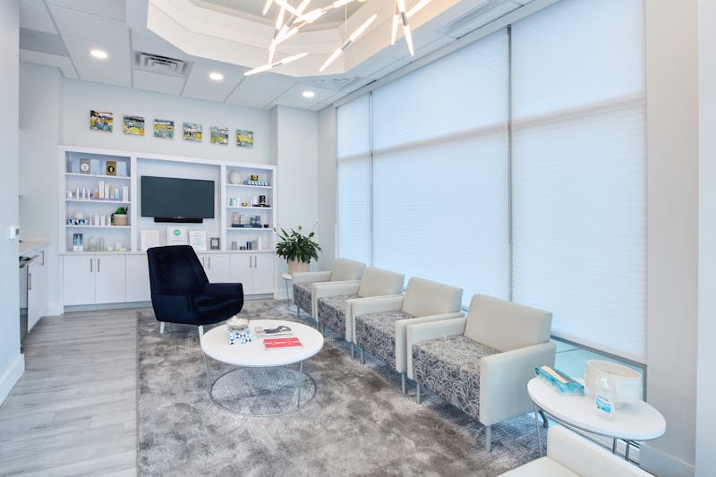 waiting room area with 4 white chairs, a white round table, and tv on wall