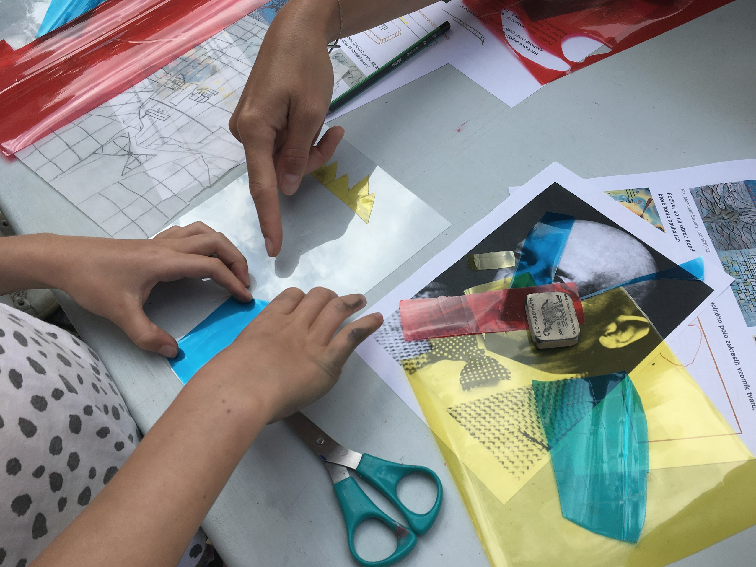 Detail dětských rukou při práci s barevnými fóliemi během výtvarného sympozia na téma Bauhaus ve Ville Pellé