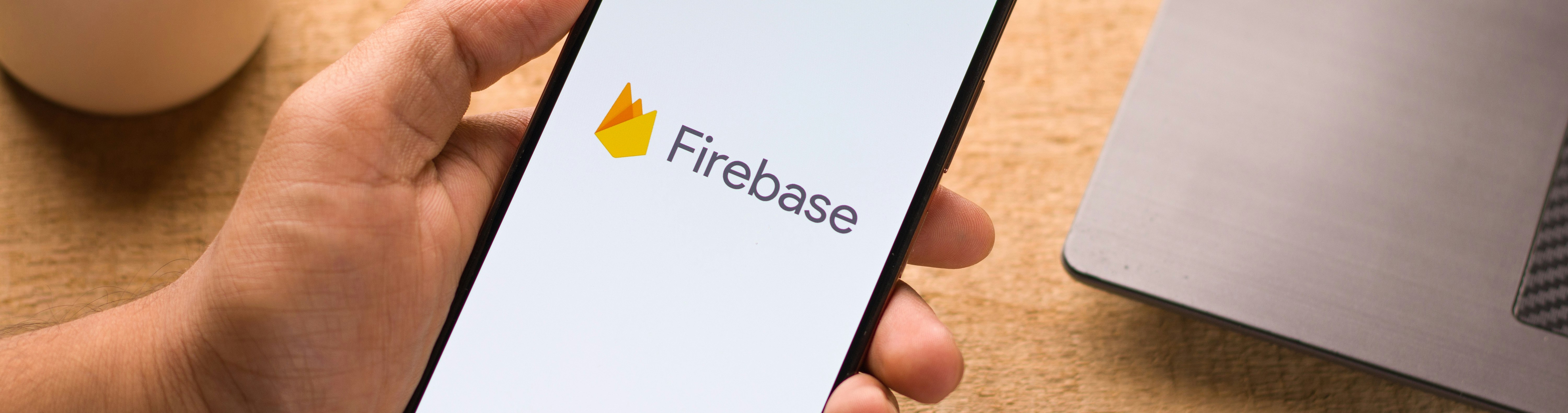 Man holding phone with Firebase logo with computer in the background