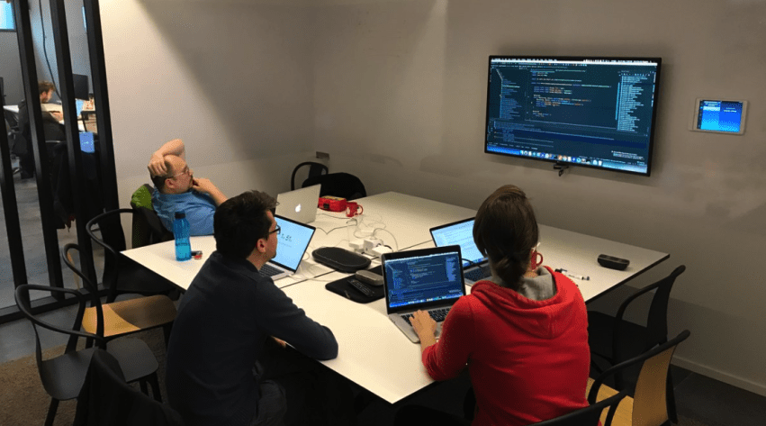 Mob programming: a team experiment blog post hero image, team sitting in meeting room developing together