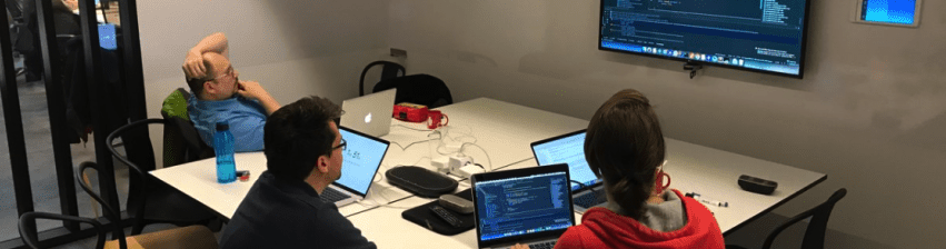 Mob programming: a team experiment blog post hero image, team sitting in meeting room developing together