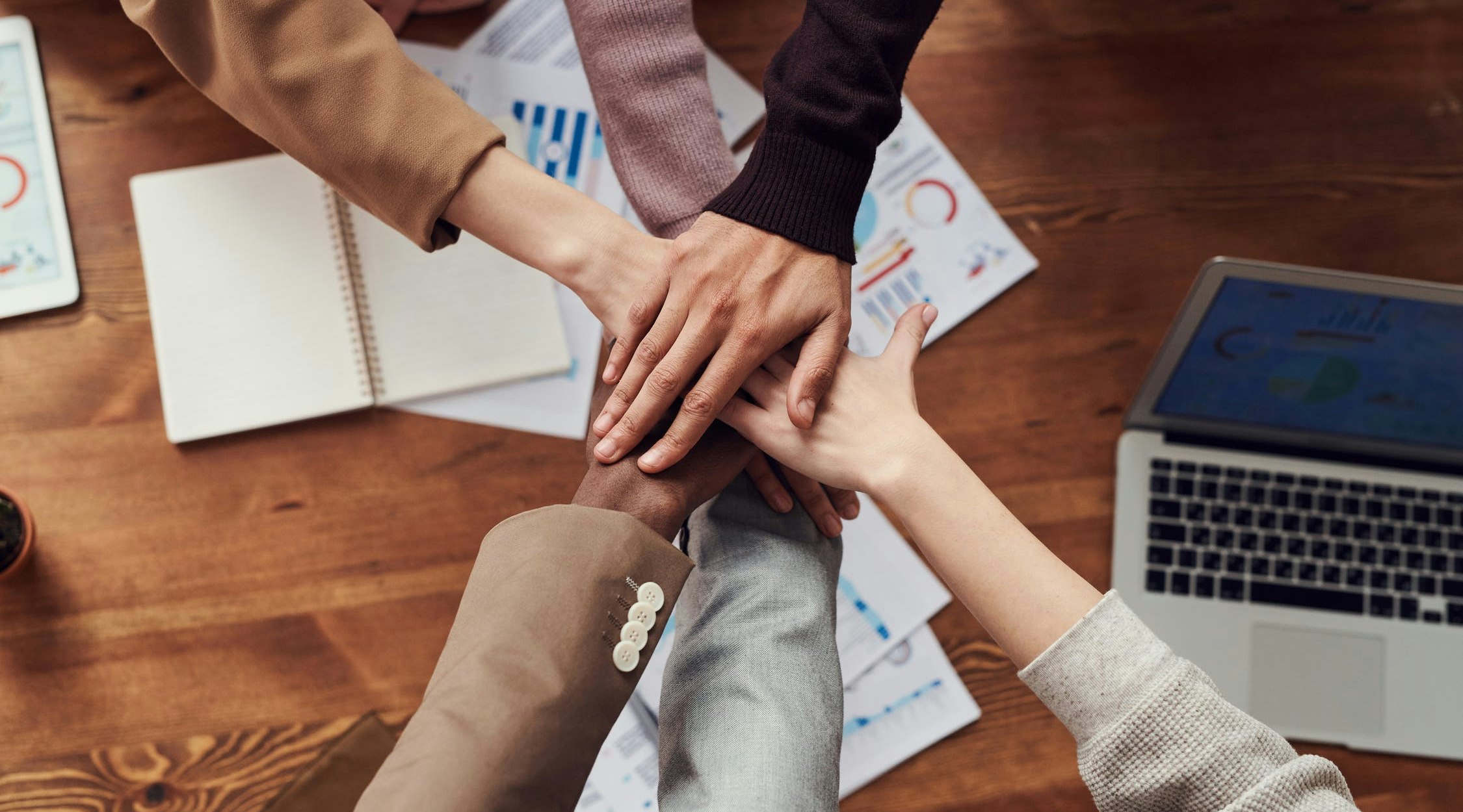 zes handen op elkaar gelegd die teamwerk aantonen