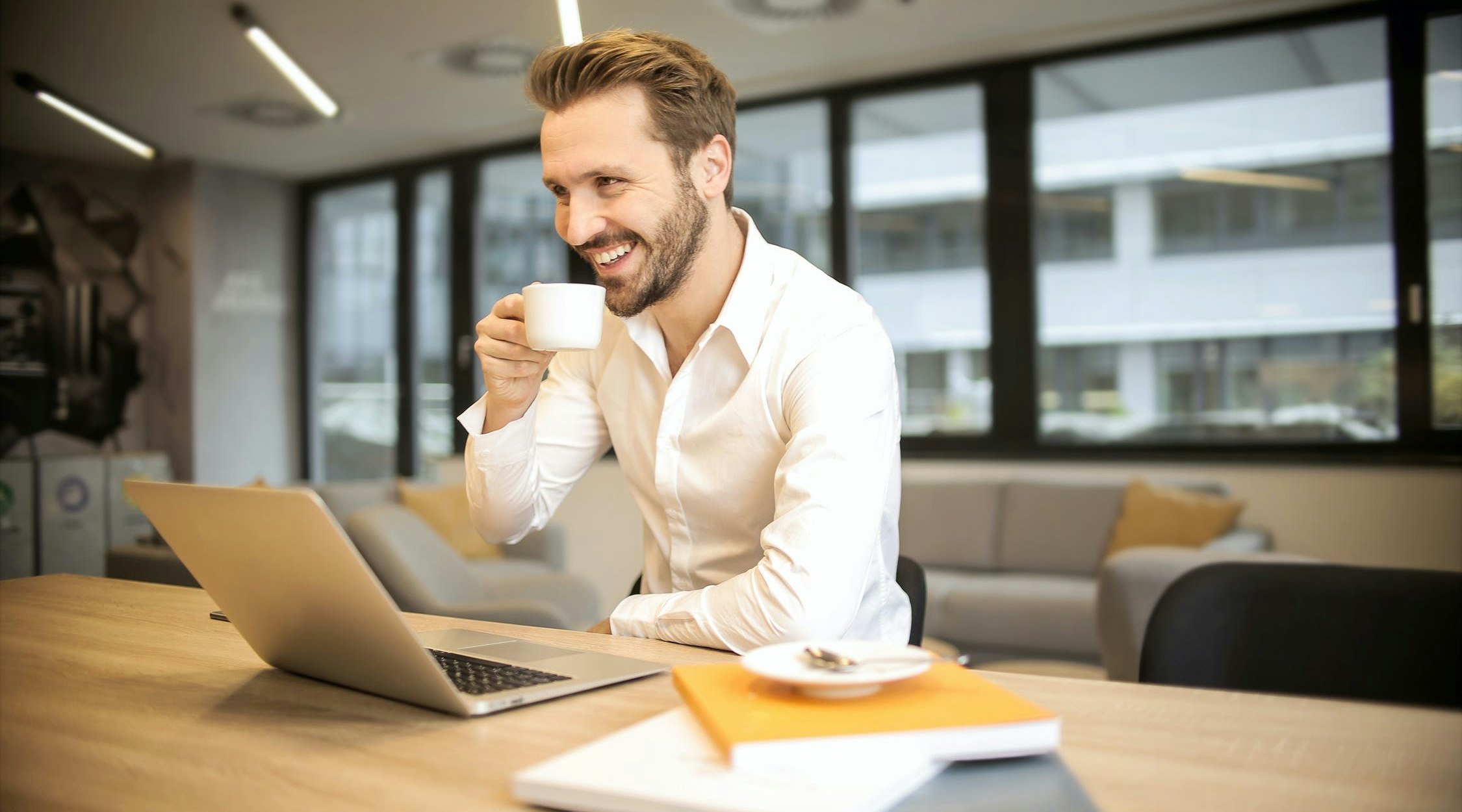 A man drinking coffee in front a laptop.