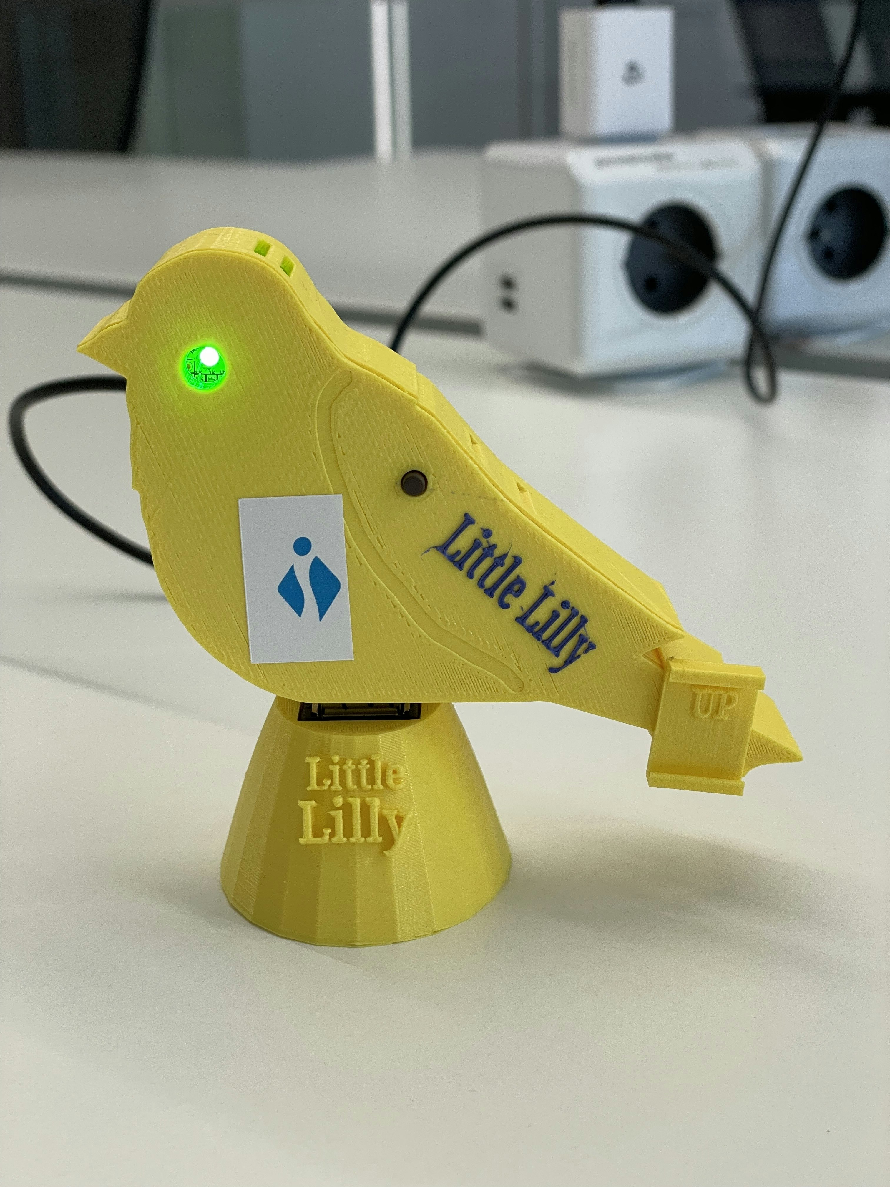 Picture of 'Little Lilly': a yellow device in the shape of a canary with a green or red LED to signal good or bad air quality around the device