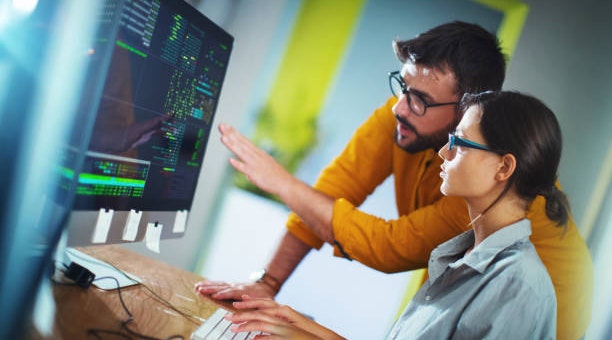 Young man and woman working together by discussing data that is on a big computerscreen.