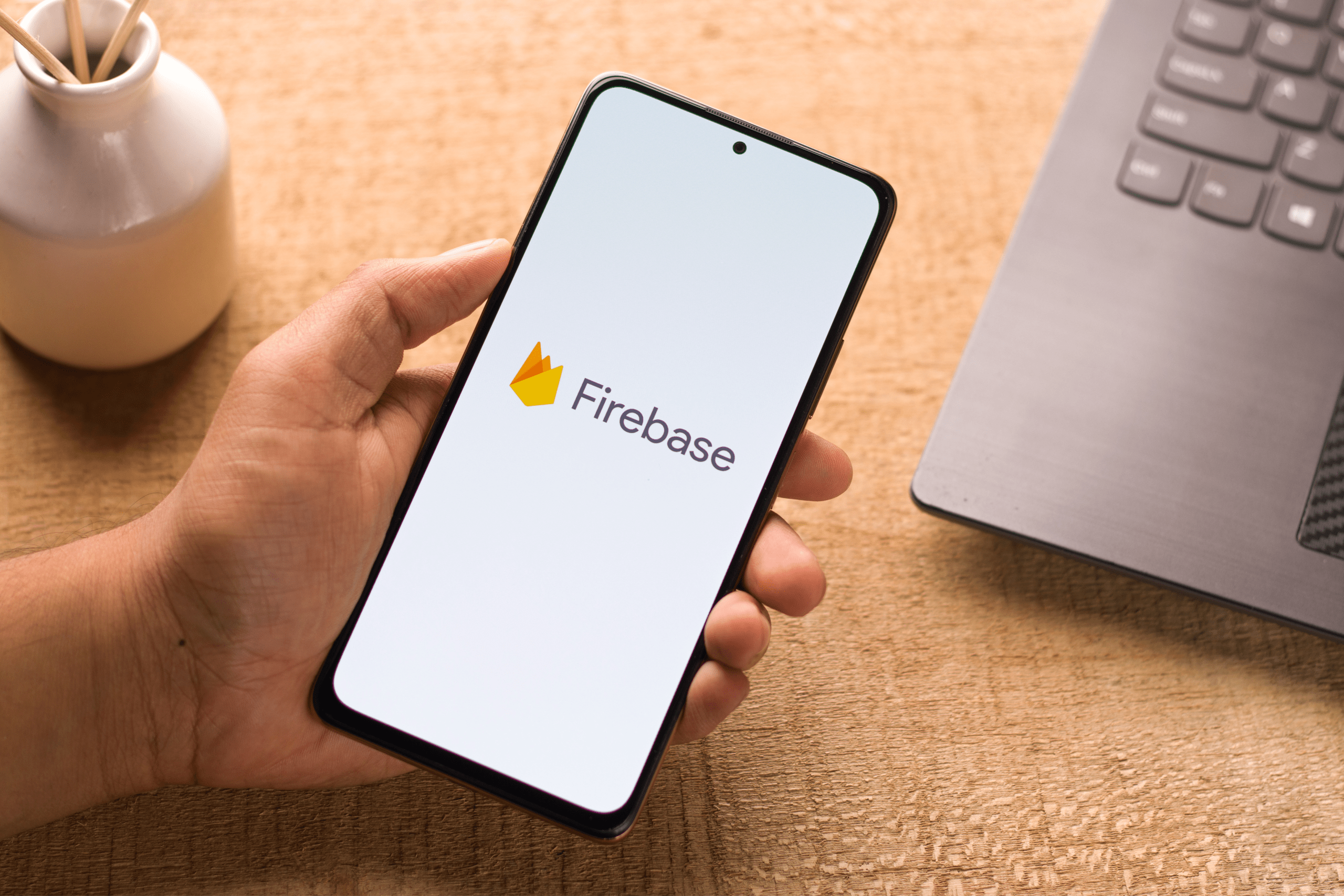 Man holding phone with Firebase logo with computer in the background