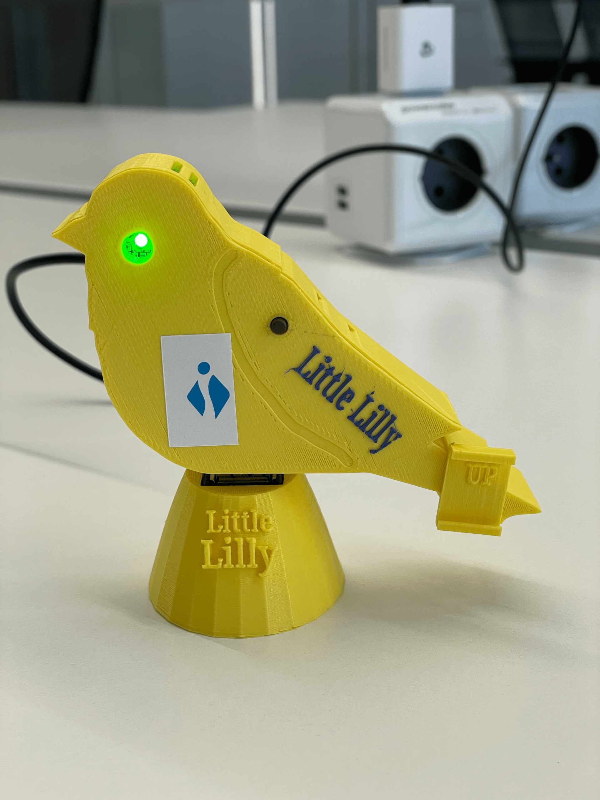 Foto van een 'Little Lilly': een geel toestelletje in de vorm van een kanarievogel met een groene of rode LED om de luchtkwaliteit rond het toestel aan te geven