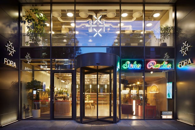An image of the outside of Fora with glass windows, rotating doors and lights.