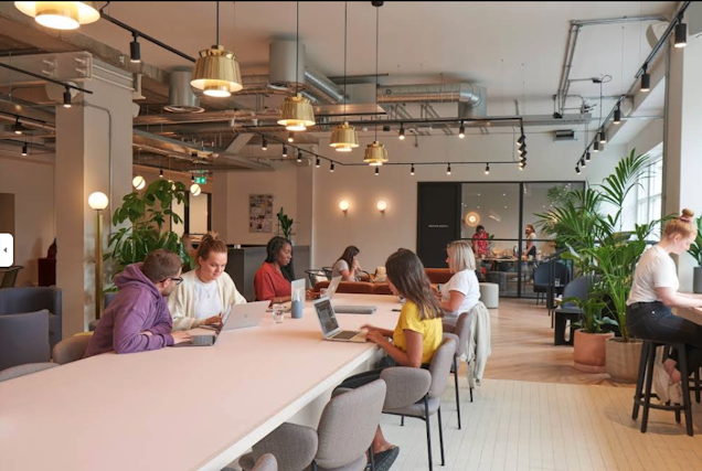 This is an image of the co-working space, a large table in the centre with a meeting room in the background.
