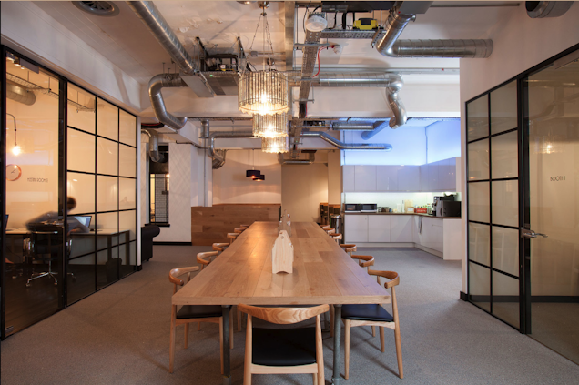 An image of a large table in a communal space and a kitchen in the background.