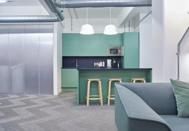 An image of a green kitchen, a couch arm in the Fora breakout space.
