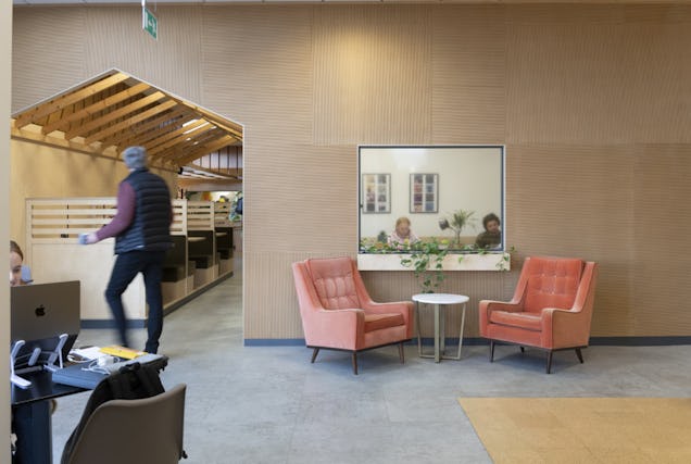 An image of a breakout space with two arm chairs and a window into a meeting room.