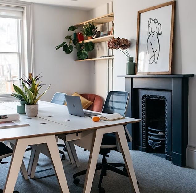 An image of an office with a fire place, trestle tables and plants.