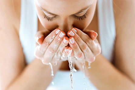Eine junge Frau reinigt ihr Gesicht mit Wasser.