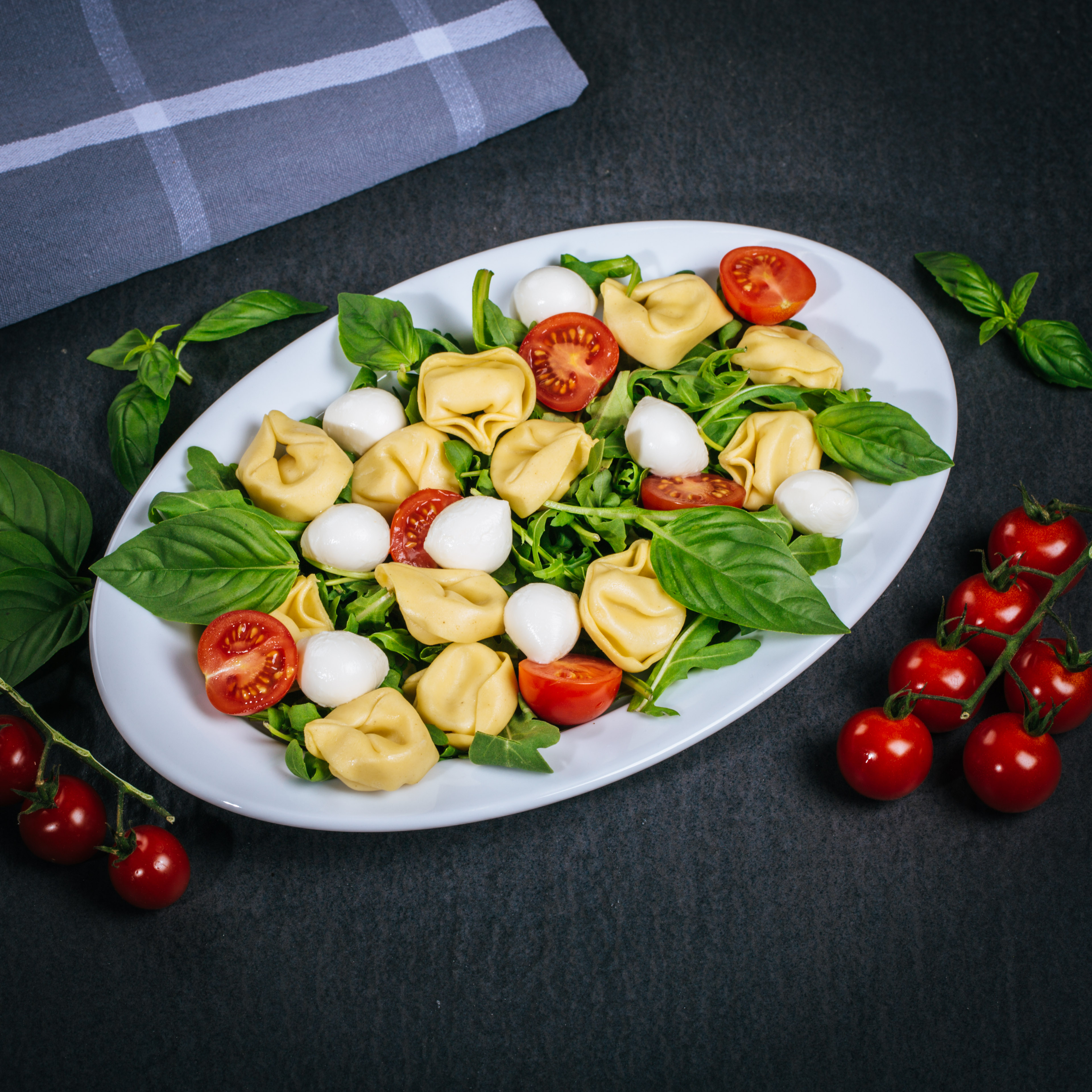 Tortellini Salat mit Cherrytomaten und Mozzarella angerichtet auf einer Platte mit Basilikum