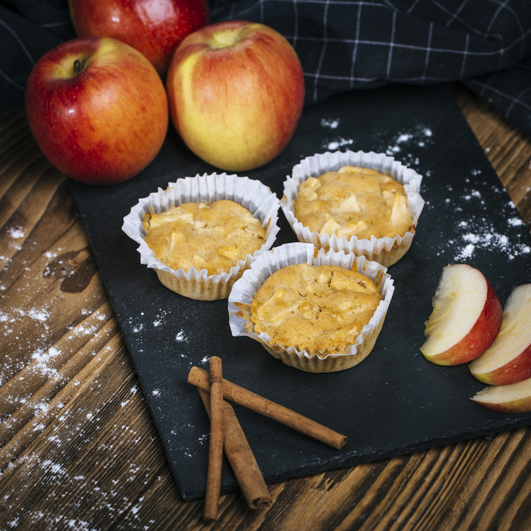 Selbstgemachte Apfel-Zim-Muffins angerichtet auf einer Schieferplatte mit Zimtstangen, und Äpfeln