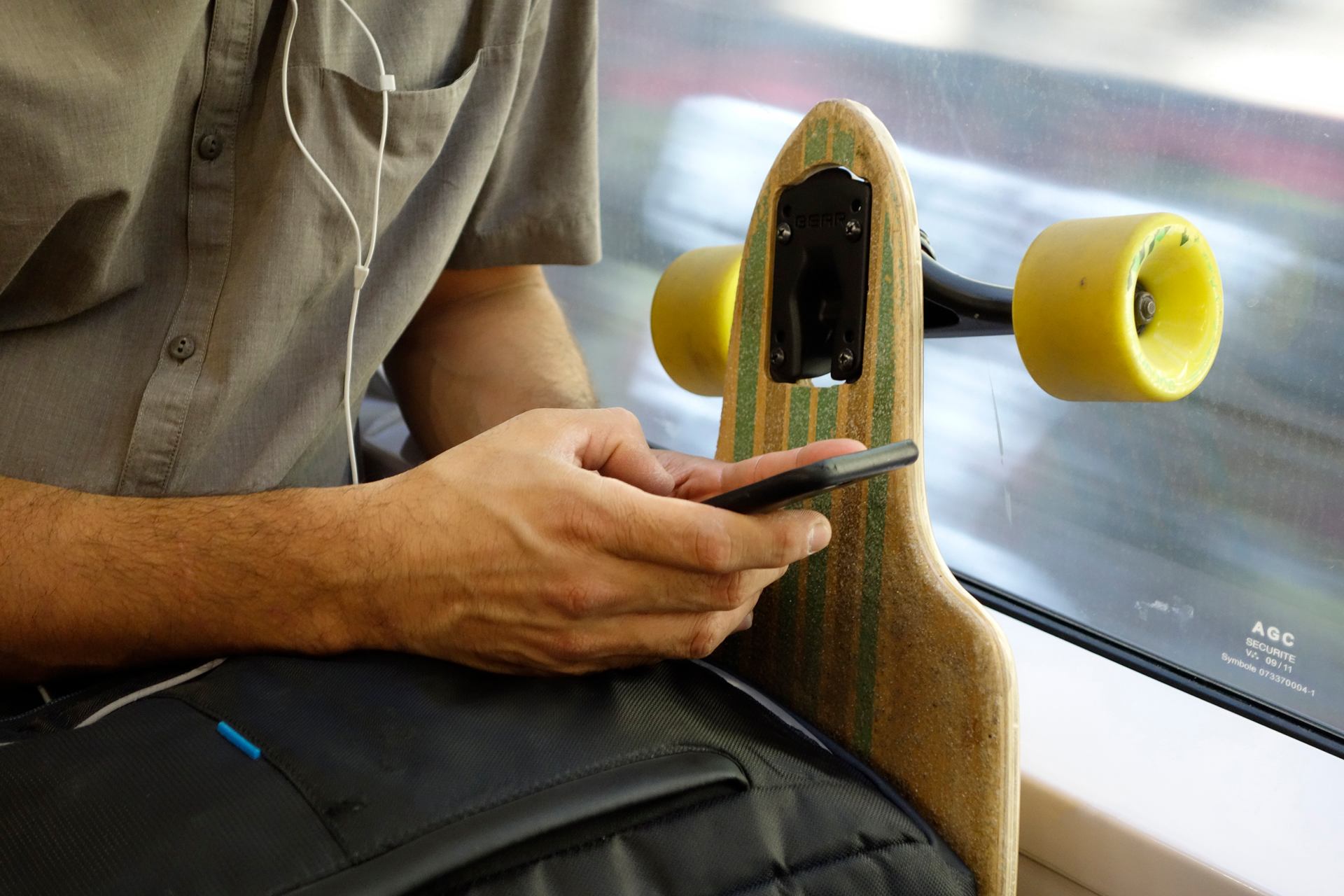 Photo d'un voyageur sur son téléphone accolé à la fenêtre avec un skateboard à coté - Lecok